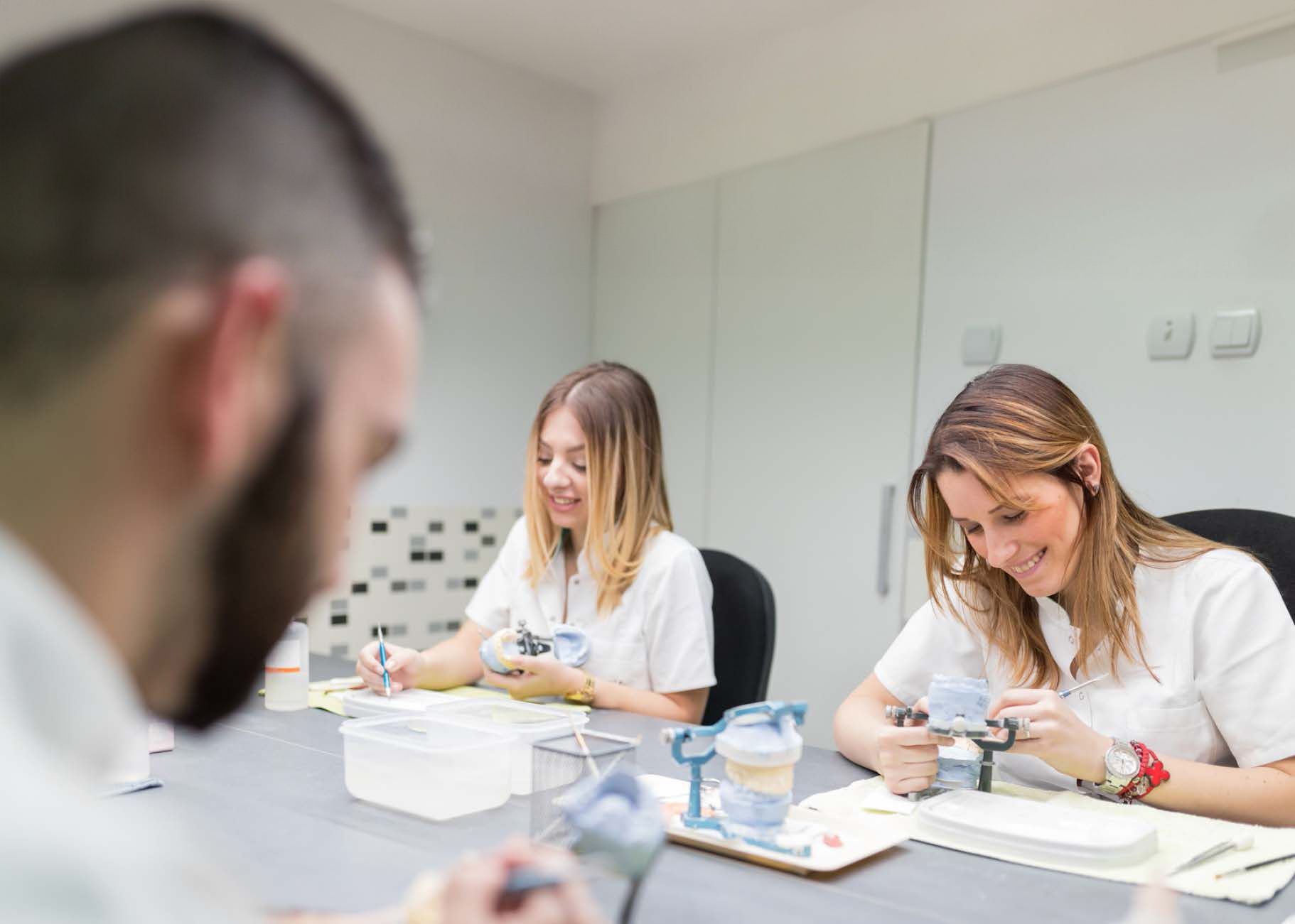 a man and two women are sitting at a table working on dental models .