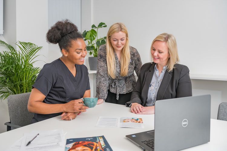 three women are sitting at a table with a laptop and a cup of coffee .
