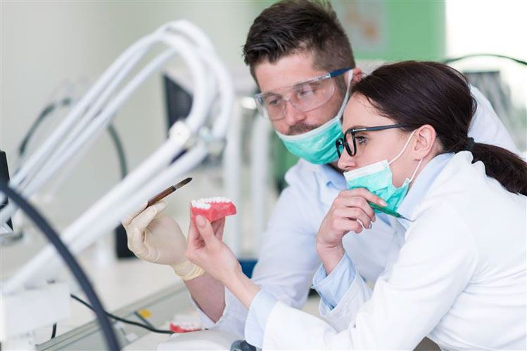 a man and a woman are looking at a model of teeth in a laboratory .
