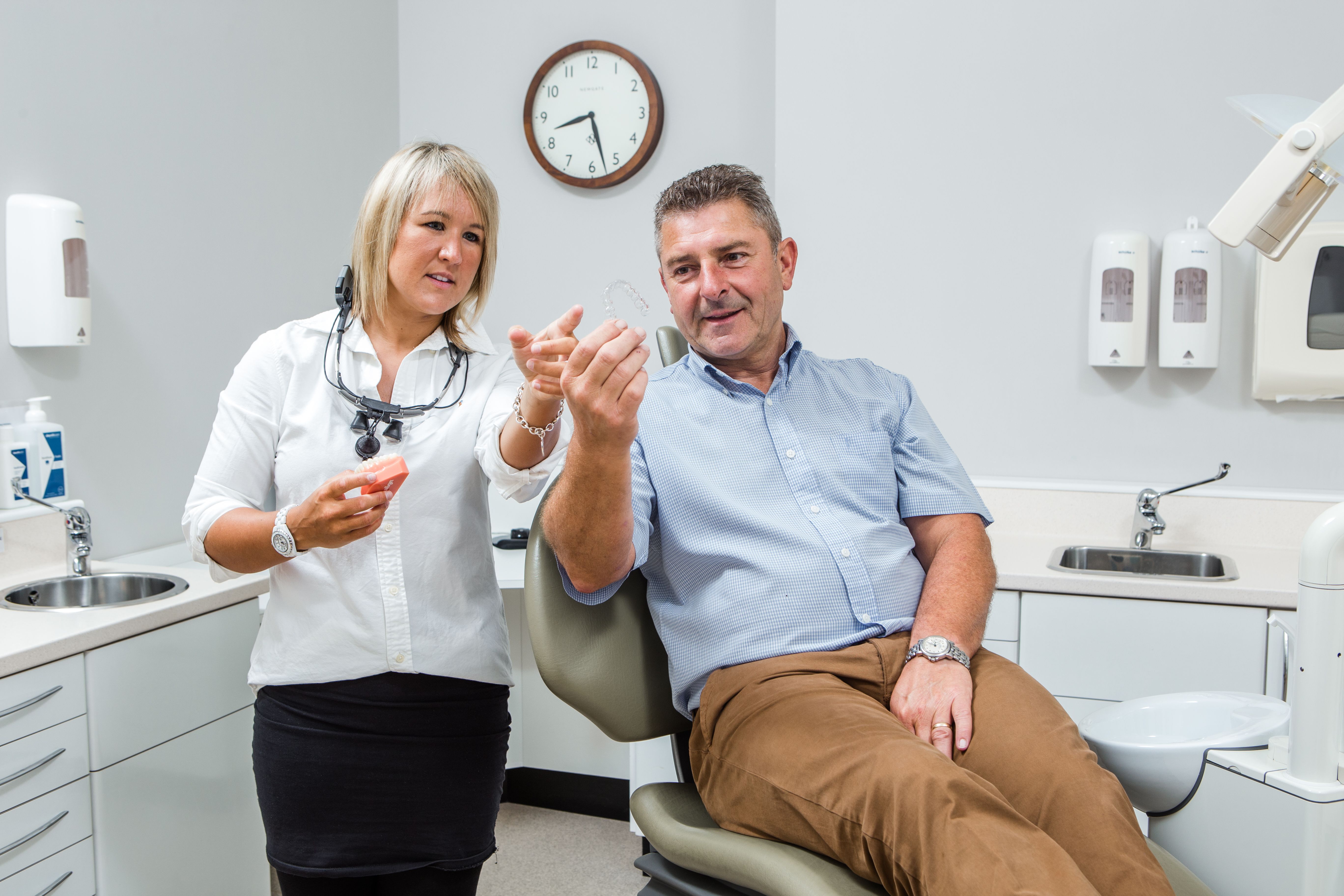a man is sitting in a dental chair while a woman stands next to him .