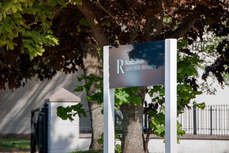 a sign for rosconnor specialist dentistry is sitting under a tree .