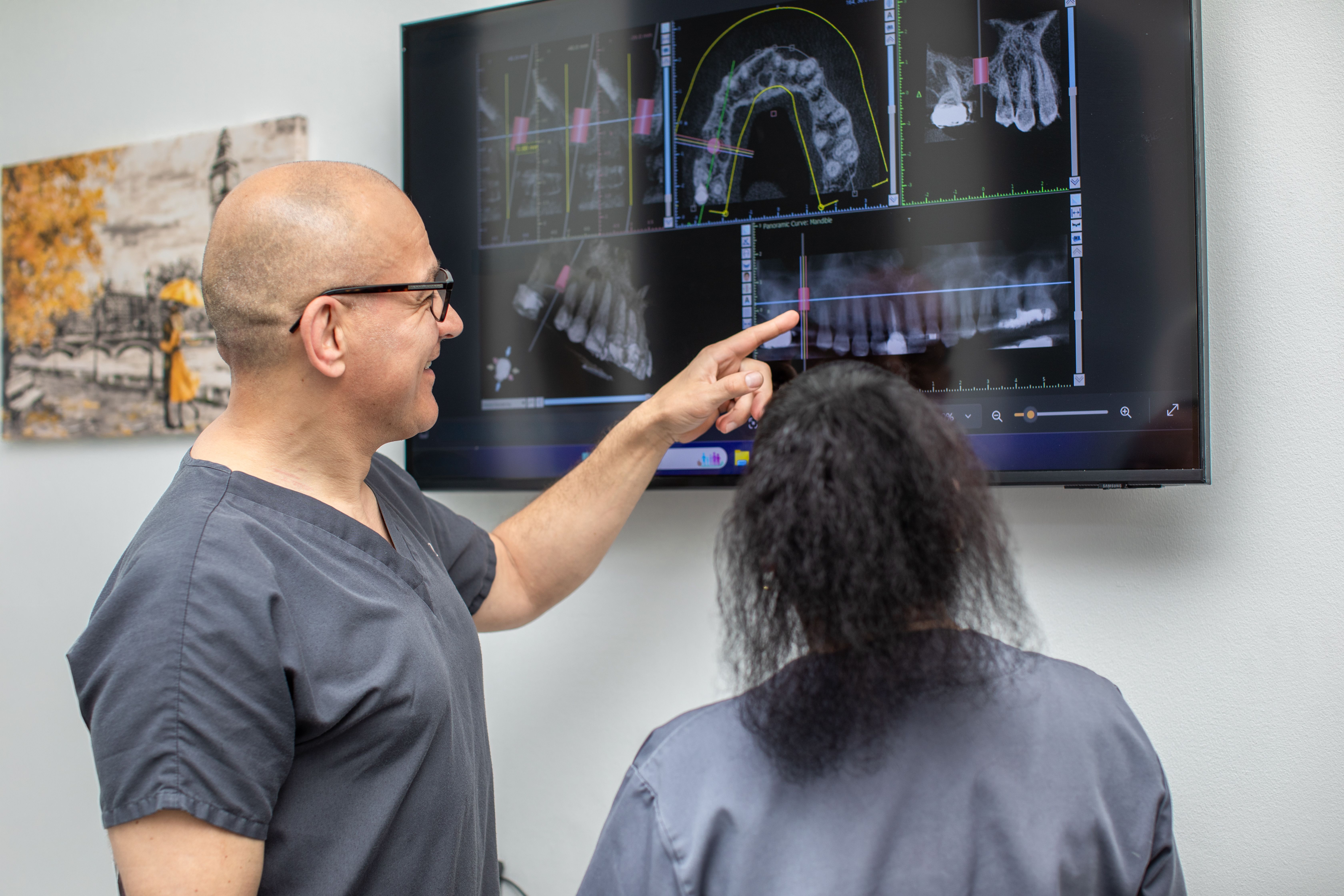 a dentist is pointing at an x-ray of a patient 's teeth on a television screen .