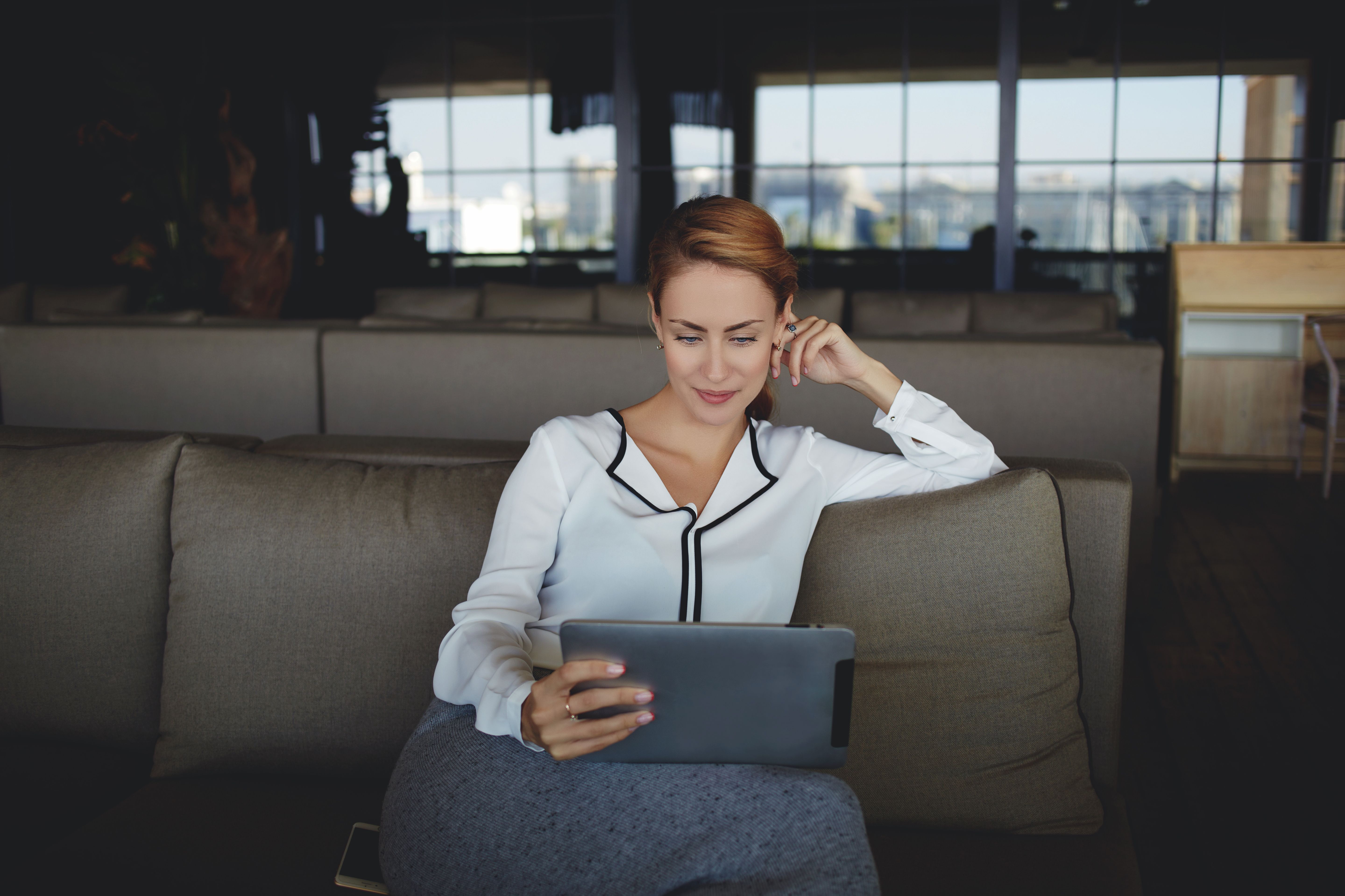 a woman is sitting on a couch using a tablet computer .