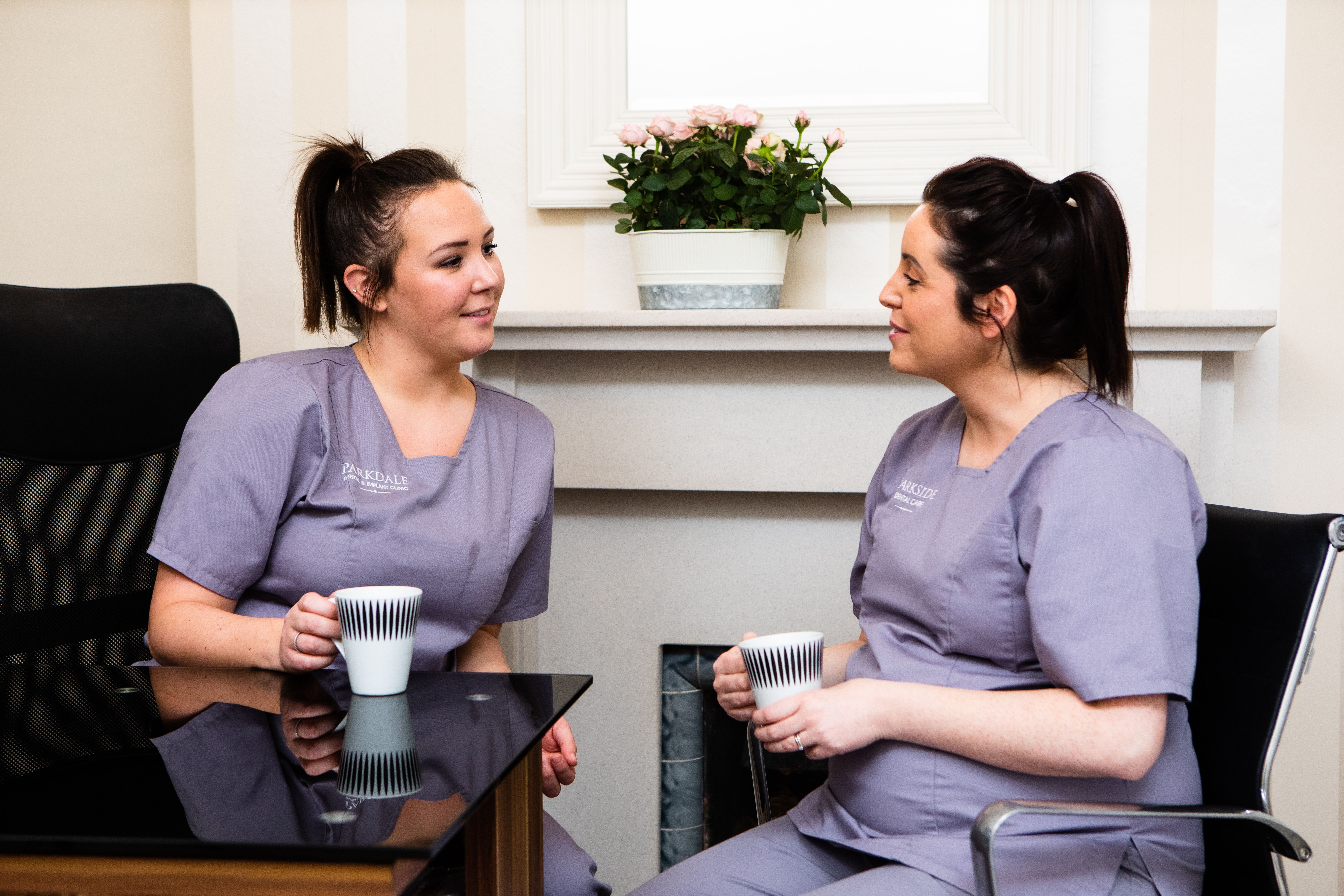 two nurses are sitting at a table drinking coffee and talking to each other .
